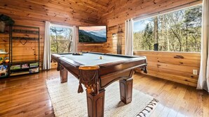 A wooden cabin with a pool table, a television, and a view of the forest. - 3 Bedroom, Sleeps 10, Close to town w Pool, Hot Tub, Sauna and Game Room! (Sevierville)