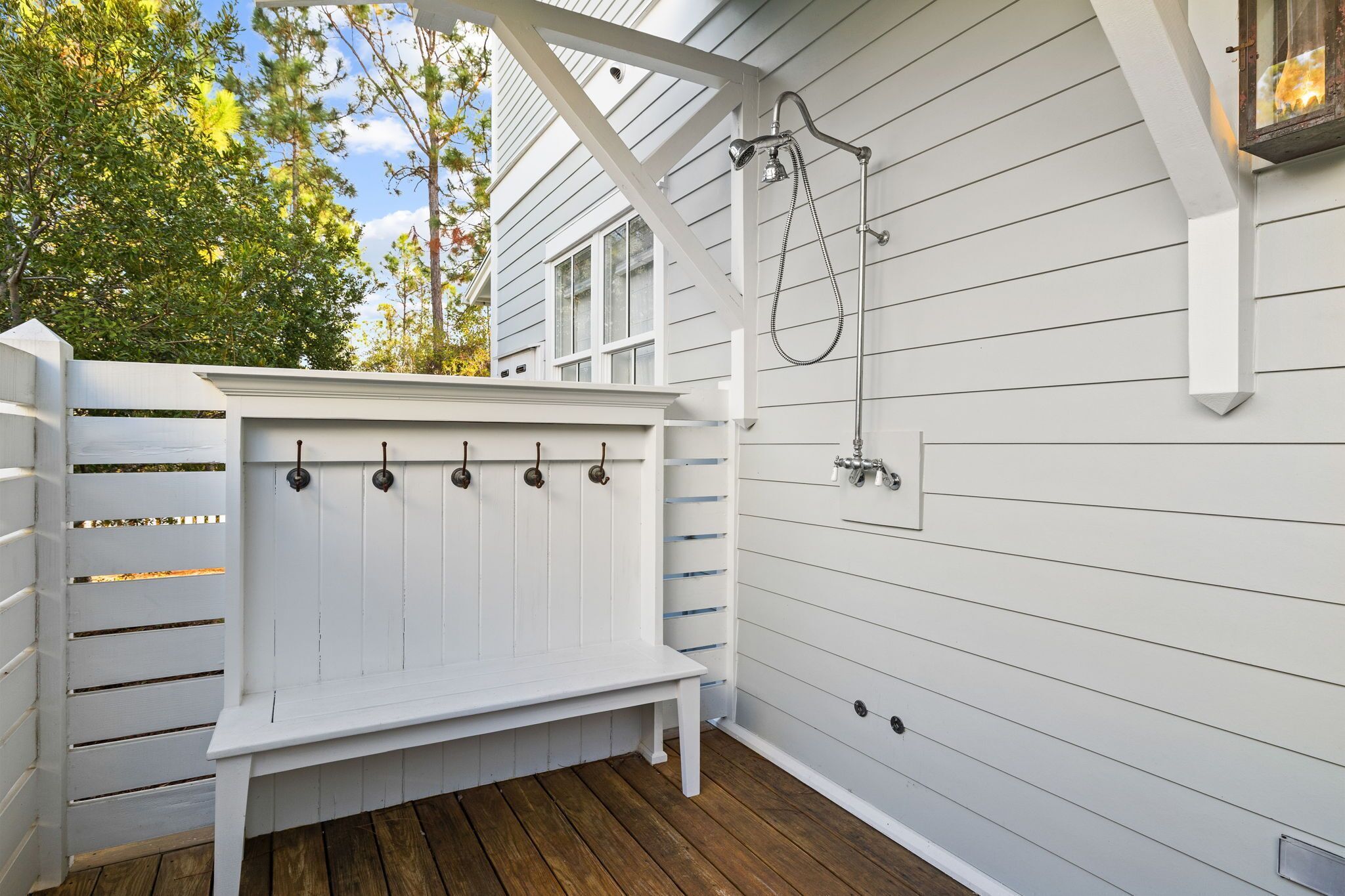 A white wooden deck with a bench, a metal showerhead, and a wall-mounted light fixture.