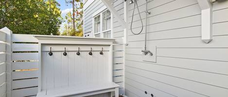 A white wooden deck with a bench, a metal showerhead, and a wall-mounted light fixture.