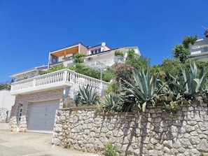 Un immeuble résidentiel avec un mur en pierre, une porte de garage blanche et un balcon doté d’une balustrade.