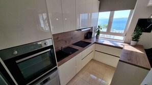 Uma cozinha moderna com armários brancos, bancada preta e vista para o mar.