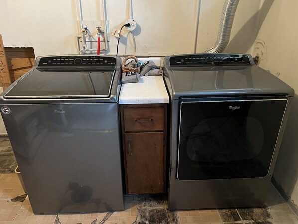 Lavadora y secadora compactas integradas en un mueble de madera pequeño, conectadas a una toma de corriente y una manguera flexible.
