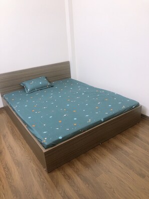 Un lit simple avec un cadre en bois et une couvre-lit turquoise ornée d’un motif sur le thème de l’espace.