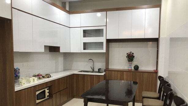 A compact kitchen with white cabinets, a black countertop, a microwave, and a sink. There is a dining table with chairs and a vase with flowers on the counter. - Selene Home (Hanoi)