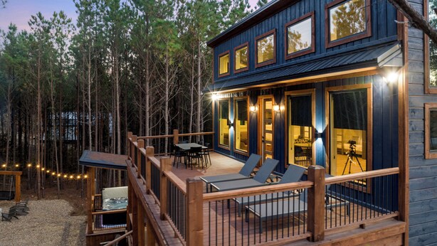 A wooden cabin with a deck, outdoor seating, and a view of the surrounding forest. - Fore Sight Golf Simulator, Games, Play-Set, Pets, Tee It Up (Broken Bow)