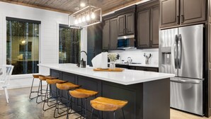 A modern kitchen with dark cabinets, a stainless steel refrigerator, and a large island with bar stools. - Fore Sight Golf Simulator, Games, Play-Set, Pets, Tee It Up (Broken Bow)