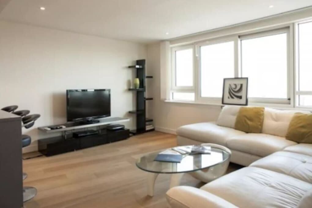 A modern living room with a flat-screen TV, a glass coffee table, and a white sofa.