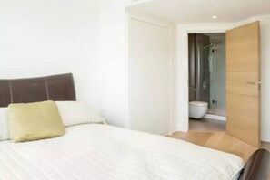 A bedroom with a bed, a wooden door, and a bathroom visible through an open door. - Fantastic Modern 2BD Flat in Centre (London)