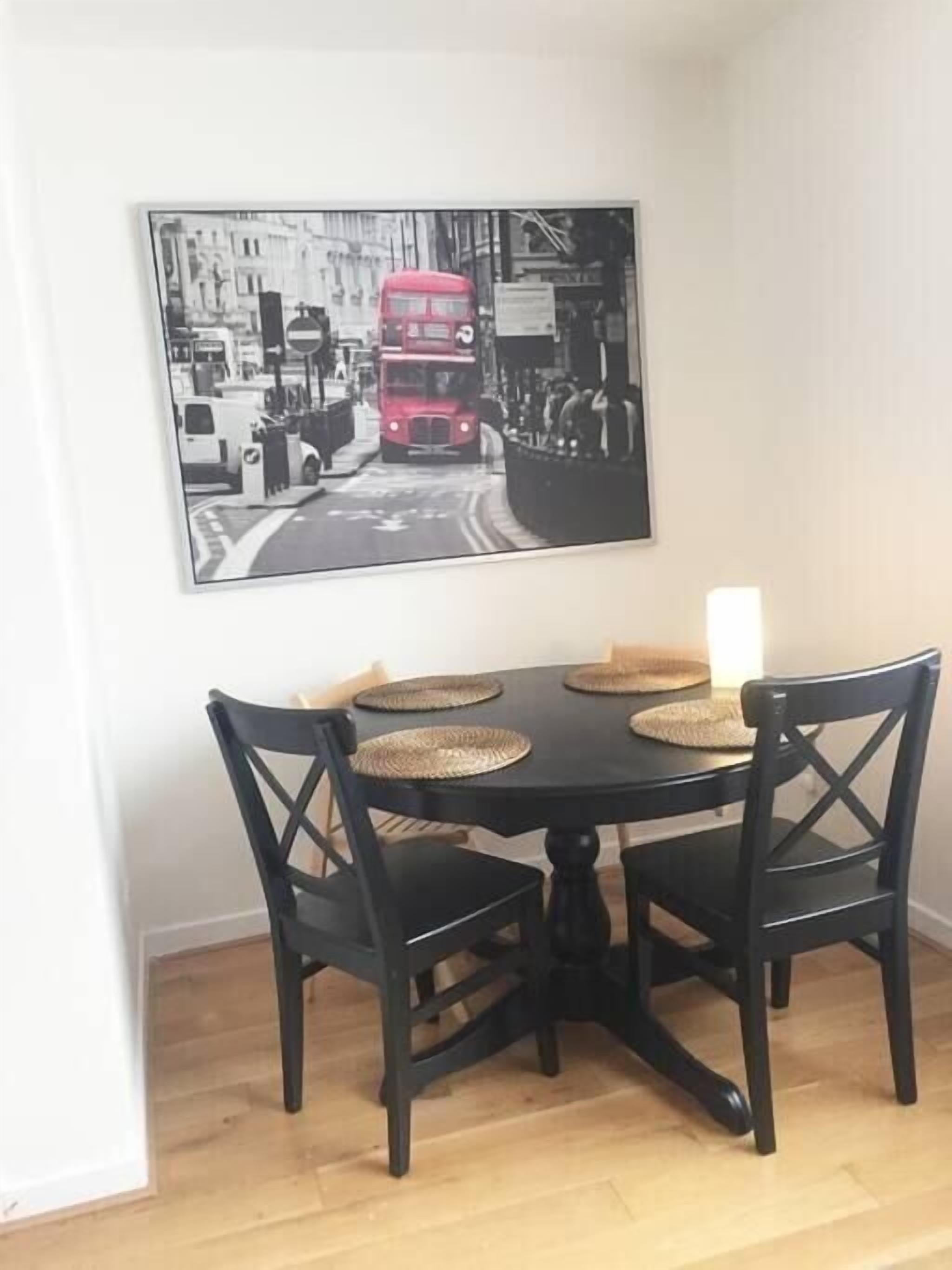 A dining area with a black table and chairs, a framed cityscape picture, and a white candle on the table.