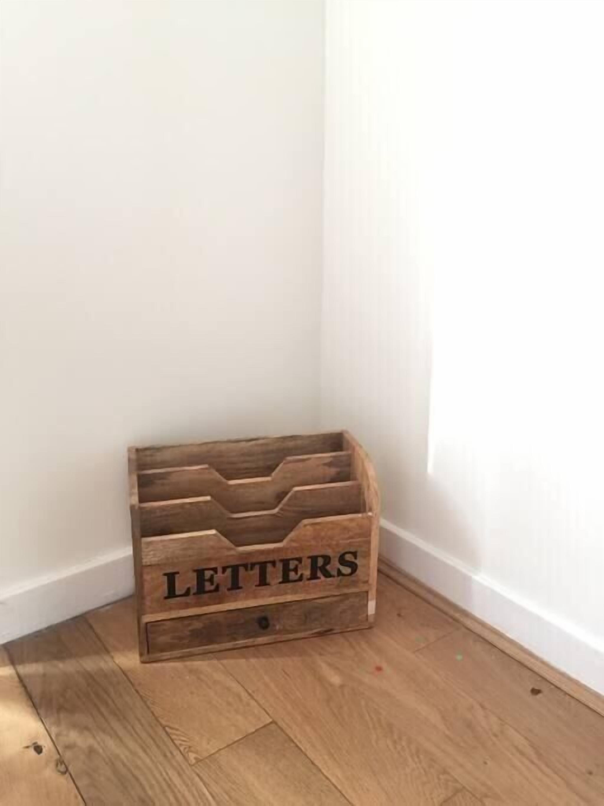 Ein Holzkoffer mit dem Aufdruck 'LETTERS' und mehreren Fächern, platziert auf einem Holzboden vor einer weißen Wand.