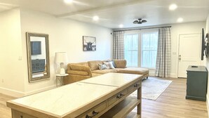 A spacious living room with a large wooden table, a sofa, and a window with curtains.