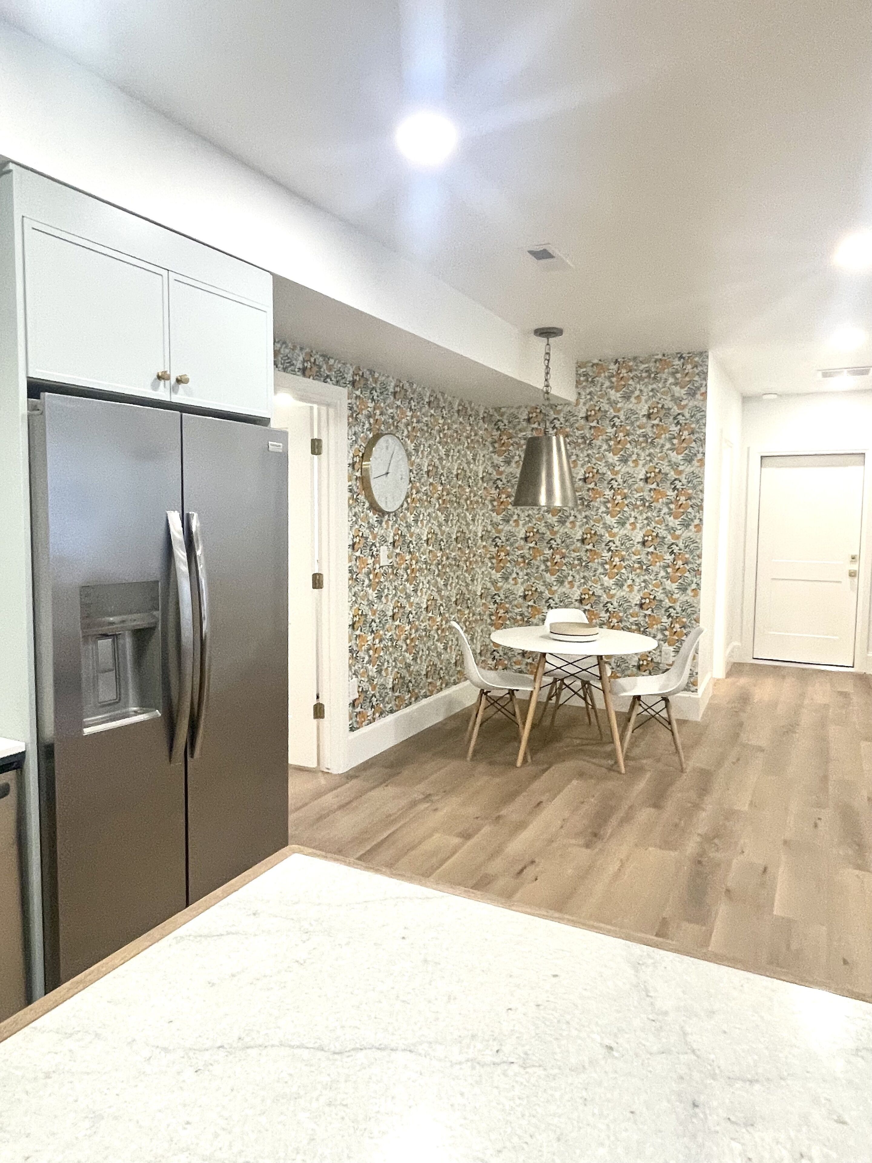 Una cocina con un refrigerador de acero inoxidable, una mesa de comedor con sillas y un papel tapiz estampado.