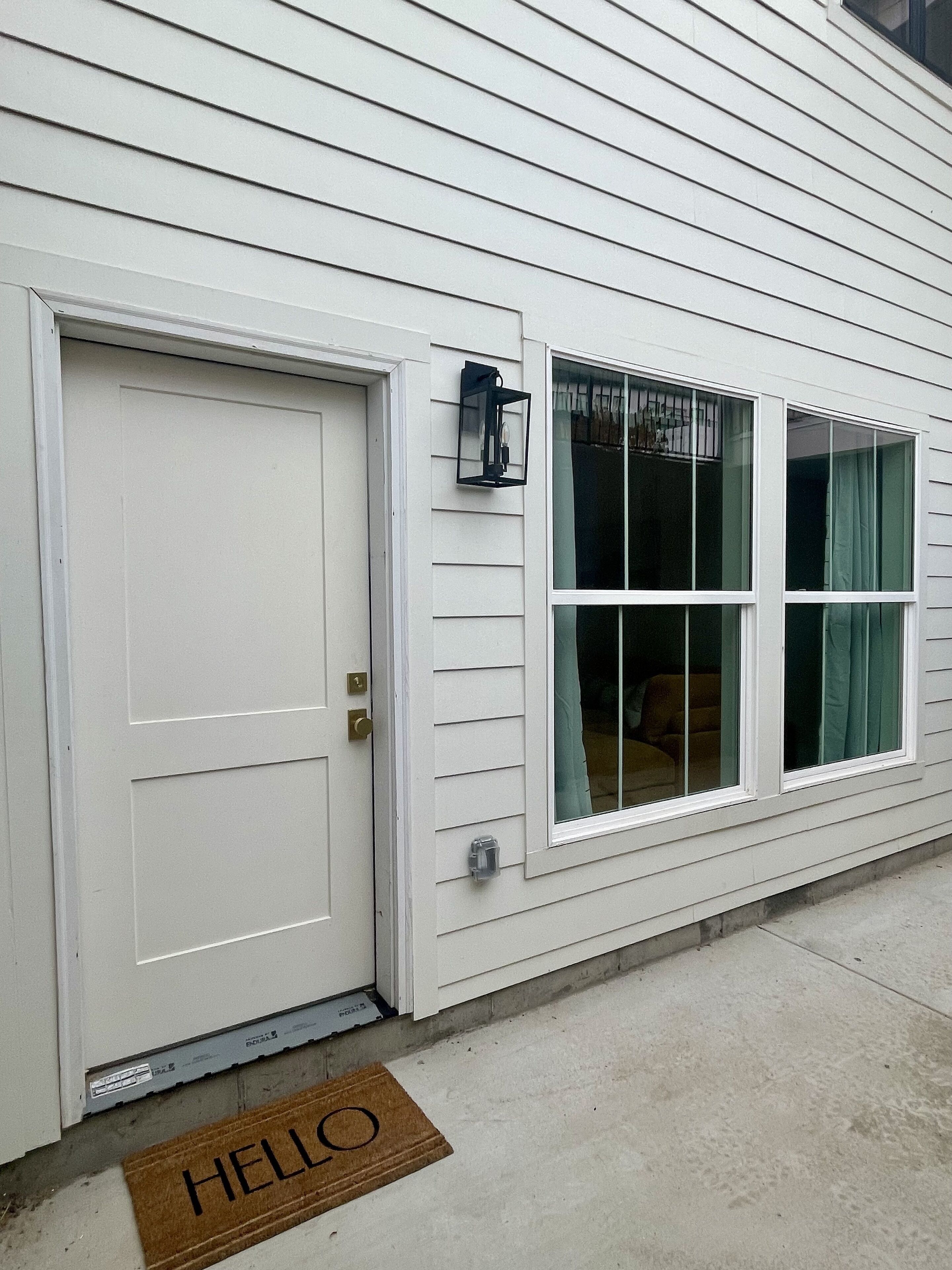 A white house with a front door, a window with curtains, and a 'HELLO' mat.