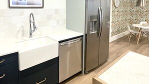 A modern kitchen with a stainless steel refrigerator, a dishwasher, and a sink. There is a dining area with a table and chairs.