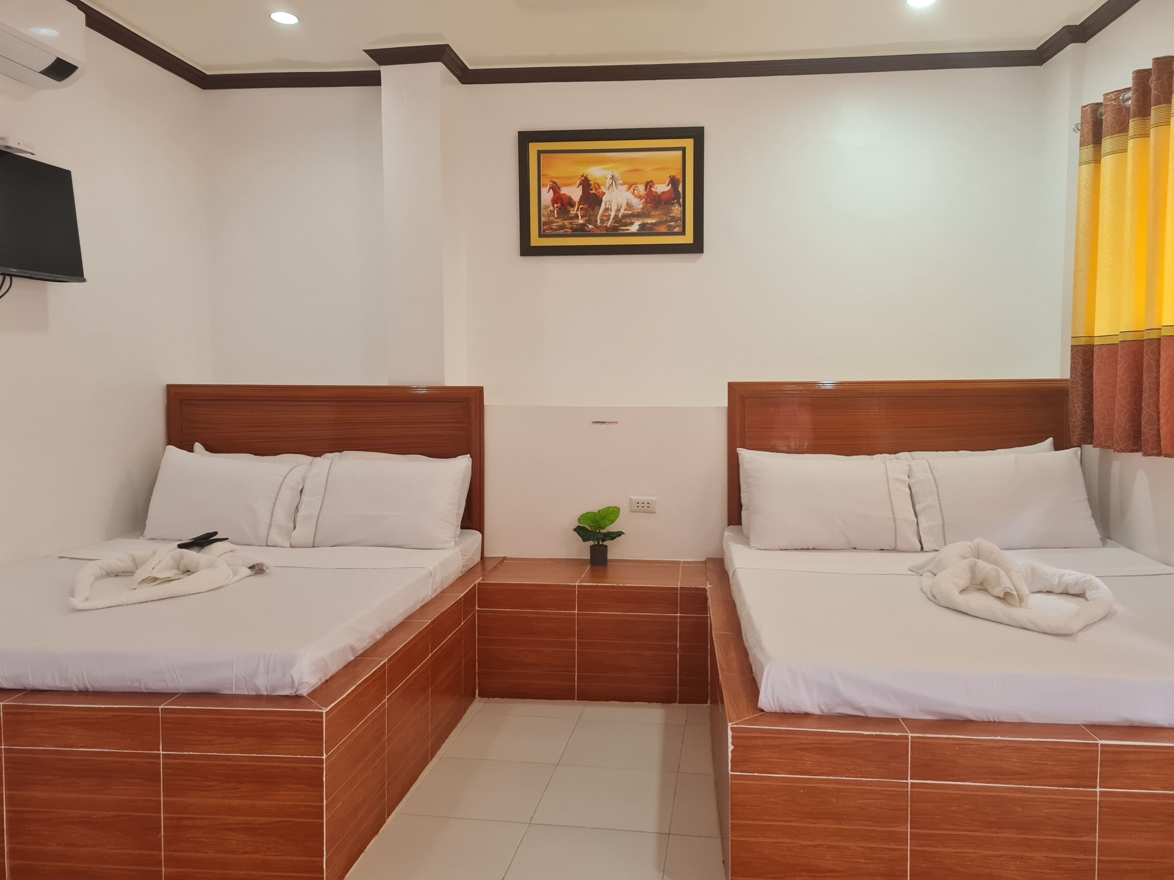 A hotel room with two beds, a TV mounted on the wall, and a painting above the beds.