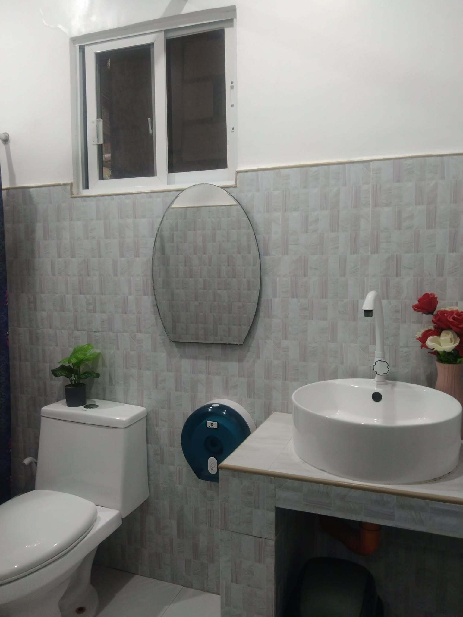 Un baño con inodoro, lavabo, ventana y espejo.