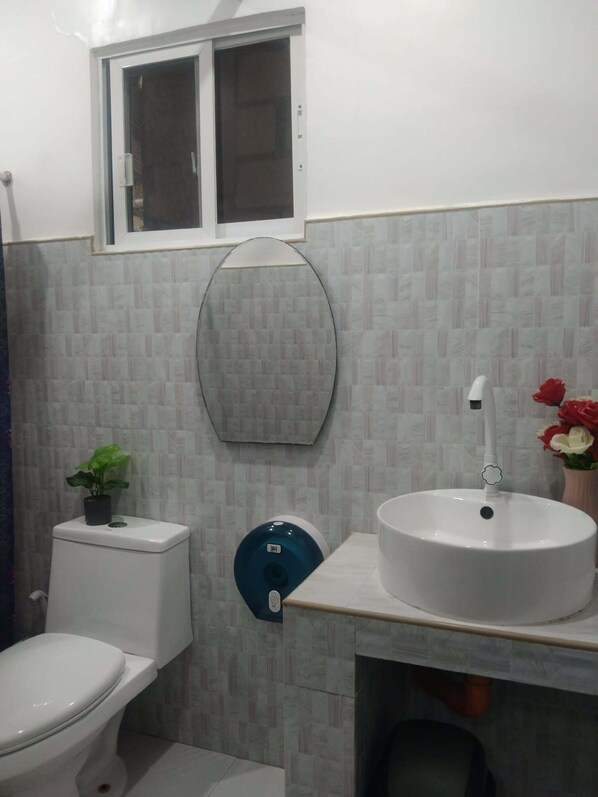 Une salle de bain avec des toilettes, un lavabo, une fenêtre et un miroir.