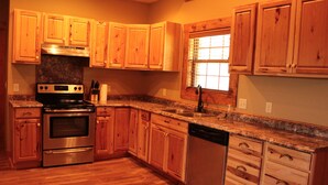 A kitchen with wooden cabinets, a stainless steel stove, a dishwasher, and granite countertops. - Cozy cabin nestled in the Ozarks with beautiful views from the front porch. (Huntsville)