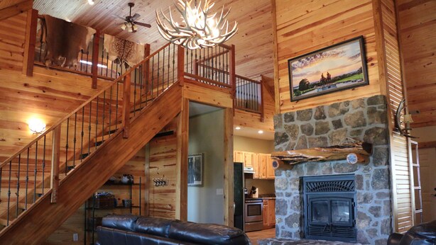A wooden interior with a stone fireplace, leather sofas, a staircase, and a dining area. - Cozy cabin nestled in the Ozarks with beautiful views from the front porch. (Huntsville)