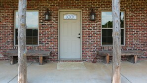 A brick building with a white door, two windows, and two benches. - Cozy cabin nestled in the Ozarks with beautiful views from the front porch. (Huntsville)