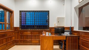 Une pièce aux murs lambrissés, comprenant un bureau, un ordinateur et une fenêtre ornée de barreaux en métal.