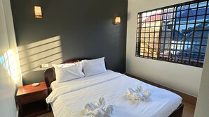 Une chambre d’hôtel avec un lit, une table de chevet, une lampe fixée au mur et une fenêtre donnant sur des immeubles.