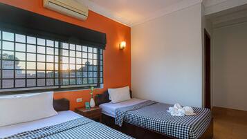A hotel room with two beds, a large window with a view, an air conditioner, and a bedside table with a vase and a clock.