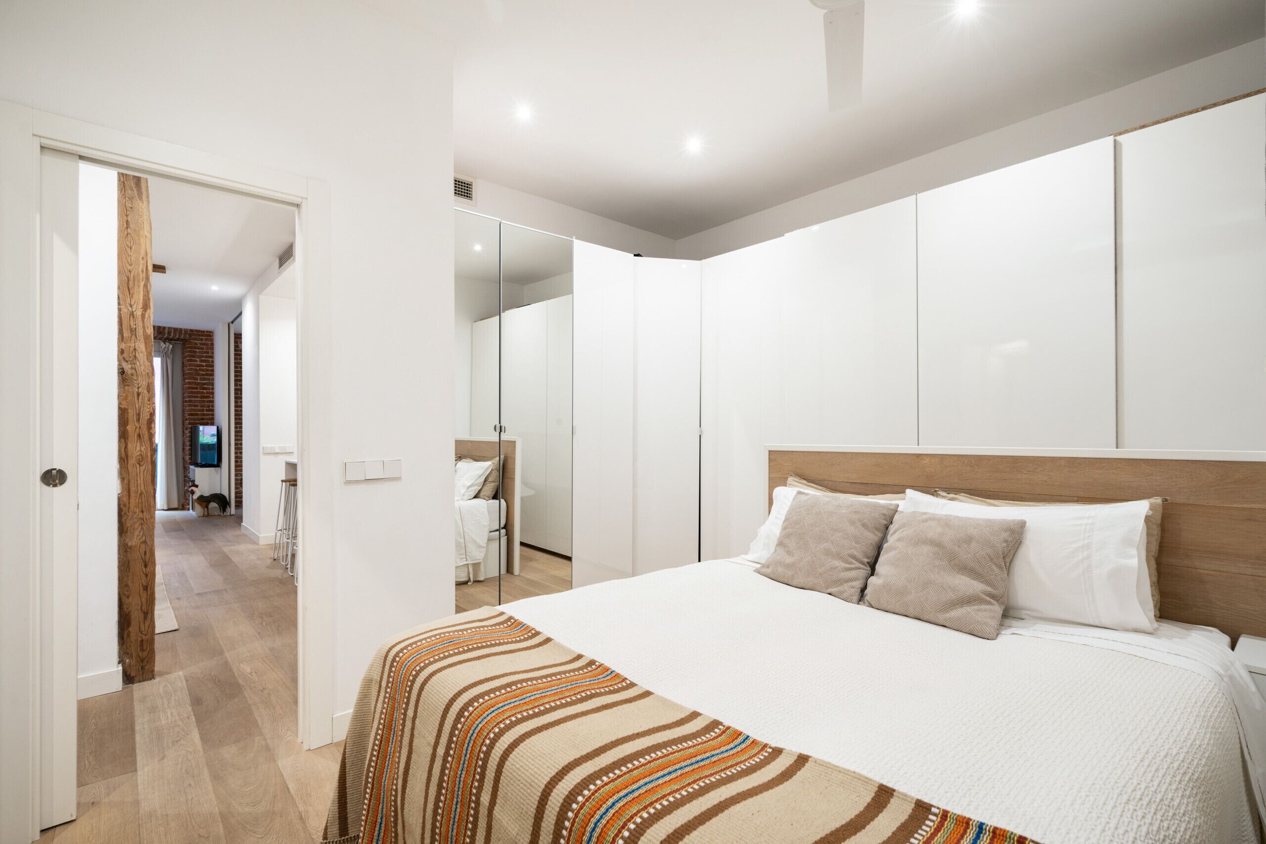 Une chambre moderne avec un grand lit, des murs blancs et une tête de lit en bois.