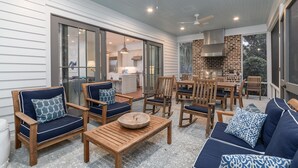 A covered patio area with wooden furniture, a brick fireplace, and a view into the kitchen. - Charming Southern Cottage near Tennis & Golf (Bluffton)