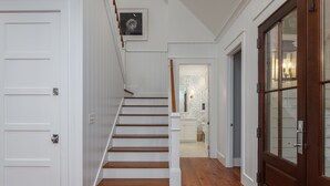 A staircase with white walls and wooden steps leading to a room with patterned wallpaper and a white door. - Charming Southern Cottage near Tennis & Golf (Bluffton)