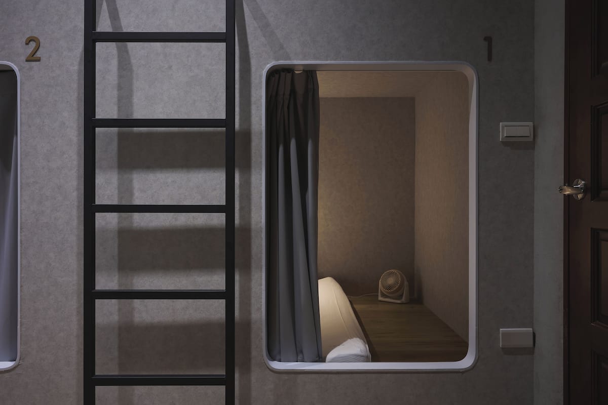 A small, private room with a bunk bed, a ladder, and a window with curtains.