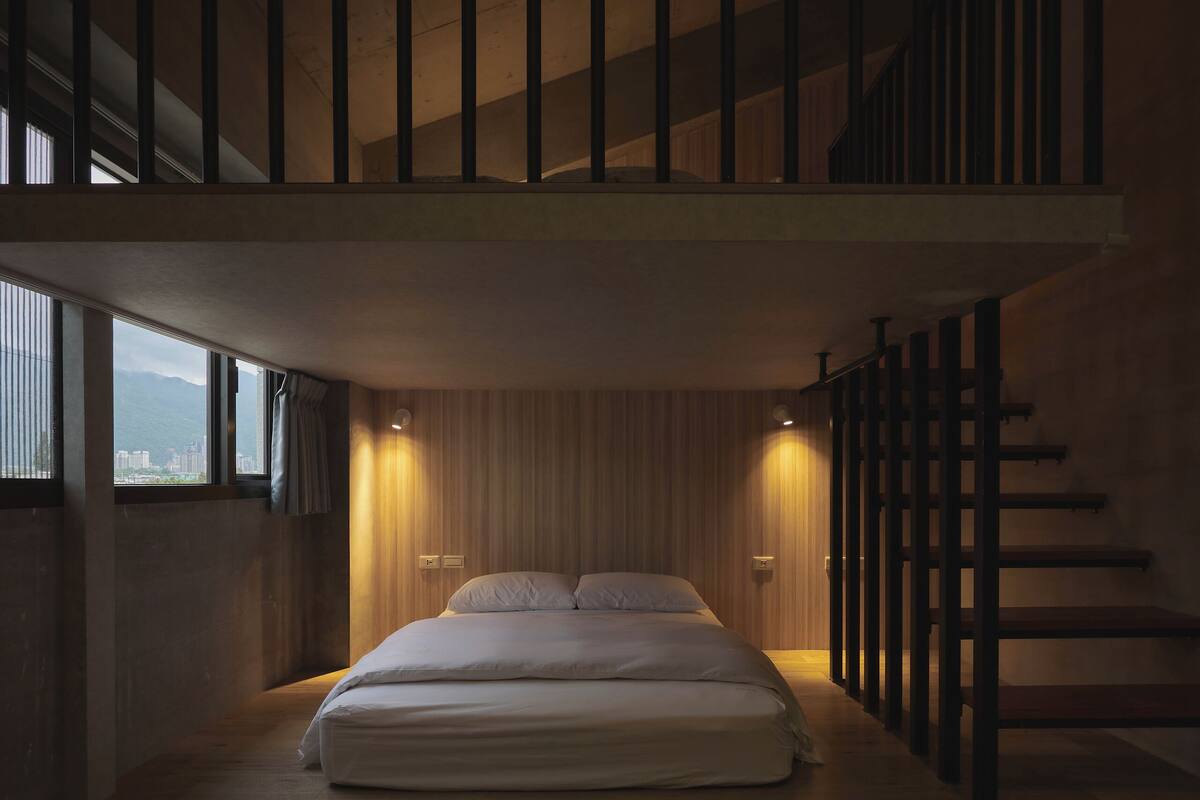 A modern bedroom with a large bed, wooden flooring, a staircase, and a city view.