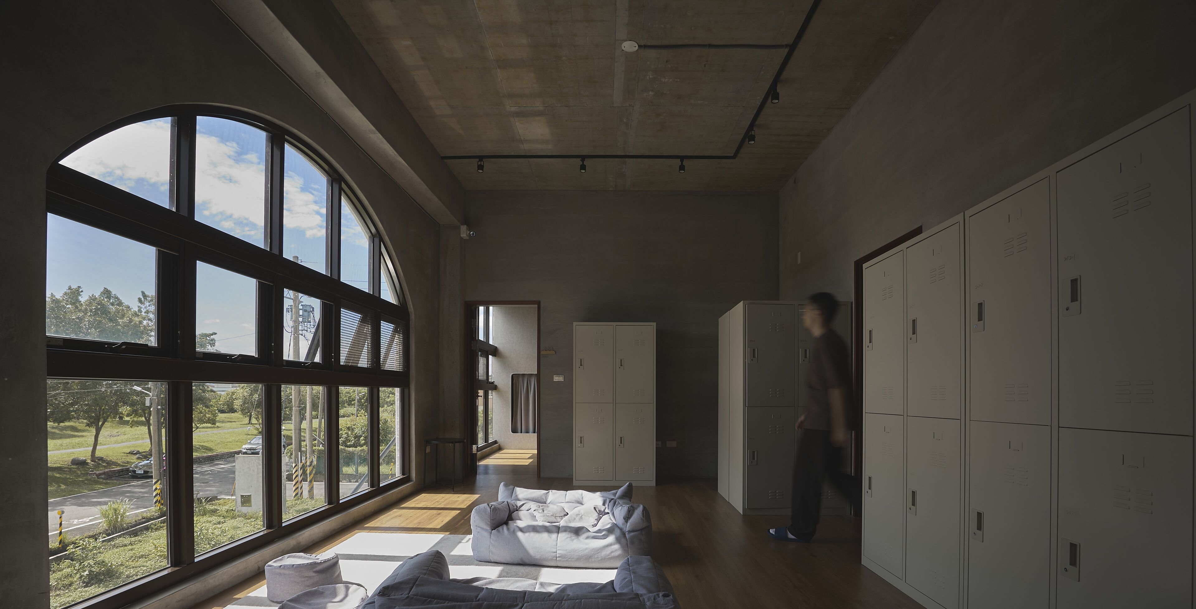 A spacious room with large windows, a sofa, and a row of lockers.