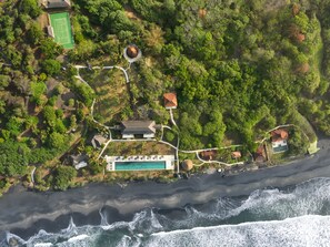 An aerial view of a coastal property with a swimming pool, tennis court, and multiple buildings surrounded by dense greenery. - Villa Leona by Nakula (Selemadeg)