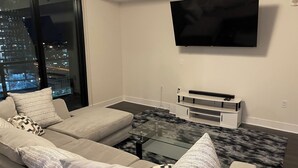 A modern living room with a large window, a flat-screen TV, a sofa, and a coffee table. - Luxurious Condo Midtown Atlanta (Atlanta)