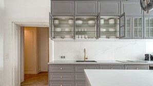 A modern kitchen with grey cabinets, a white countertop, and a built-in glass shelving unit above the sink.