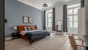 A modern bedroom with a bed, nightstands, a desk, and a large window.