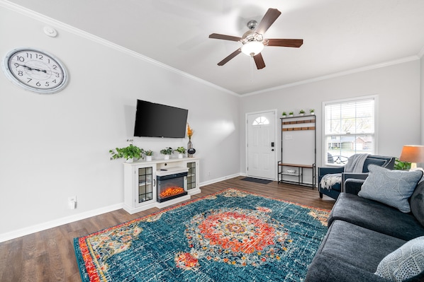 A living room with a fireplace, a ceiling fan, a television, and a large rug.