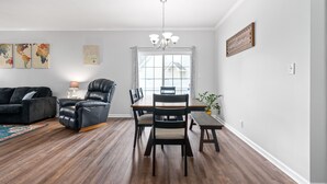 Ein modernes Wohnzimmer mit einem dunkelbraunen Ledersofa, einem schwarzen Ledersessel, einem Holzesstisch mit Stühlen, einer Kristallleuchtre und einem Wandbild einer Weltkarte.
