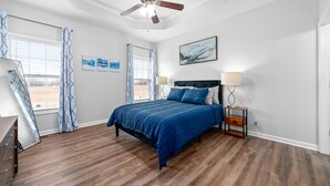 Ein Schlafzimmer mit Bett, Deckenventilator, Nachttisch und einem Vorhangfenster.