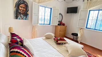 A bedroom with a bed, pillows, a dresser, a TV, and windows with curtains.