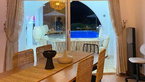 Ein Essbereich mit Tisch, Stühlen und Blick auf einen Pool im Freien bei Nacht.
