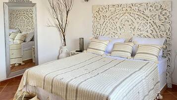 A neatly arranged bedroom with a large bed, a decorative headboard, a mirror, and a vase with branches.