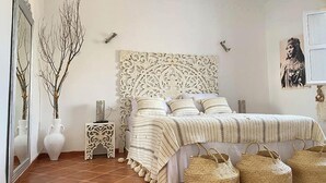 Ein Schlafzimmer mit dekorativer Kopfteil, einem Bett mit gestreifter Bettwäsche, einem Nachttisch und dekorativen Vasen.