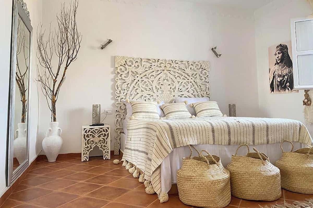 A bedroom with a decorative headboard, a bed with striped bedding, a side table, and decorative vases.