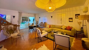 Ein Wohnzimmer mit einer Couch, Sesseln, einem Couchtisch und einer großen, gelben Hängeleuchte.