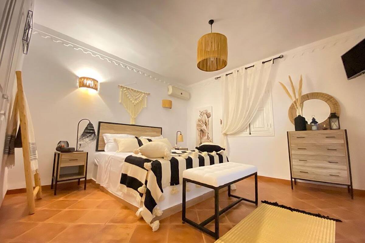 A bedroom with a bed, bedside tables, a bench, a dresser, and decorative wall art.