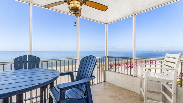 A balcony with a table and chairs, a ceiling fan, and a view of the beach.