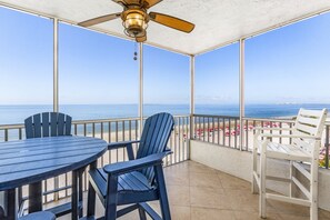 A balcony with a table and chairs, a ceiling fan, and a view of the beach. - Bay & Gulf Views | 5th Floor Condo, Pool & Walk to Times Square (Fort Myers Beach)