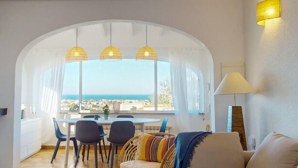 Uma sala de jantar com mesa e cadeiras, um sofá e uma luminária.